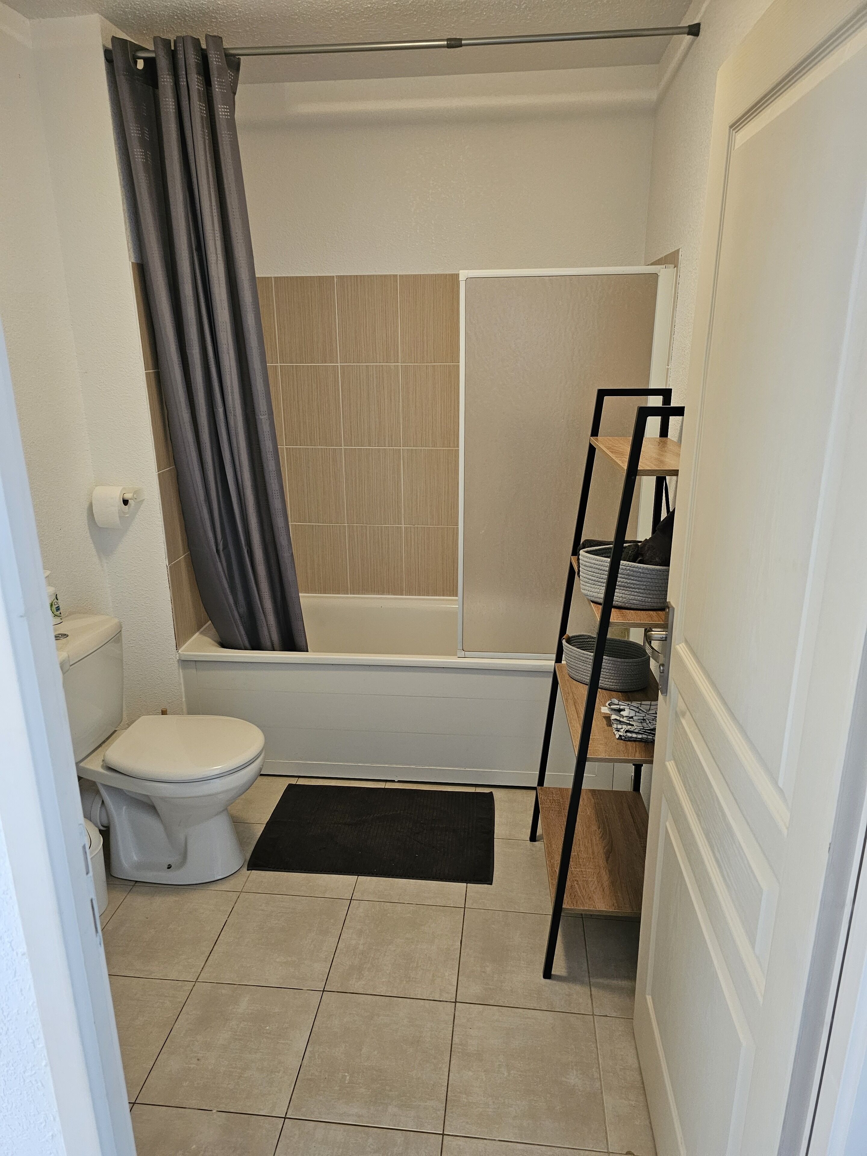 Une petite salle de bain comprenant des toilettes, une douche et une étagère avec des serviettes.