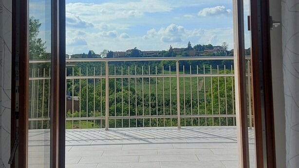 A room with a large sliding glass door leading to a balcony with a view of a green landscape and buildings in the distance. - Orchid Roero Sunsetfor couples families groups to visit Roero and Langhe (Govone)