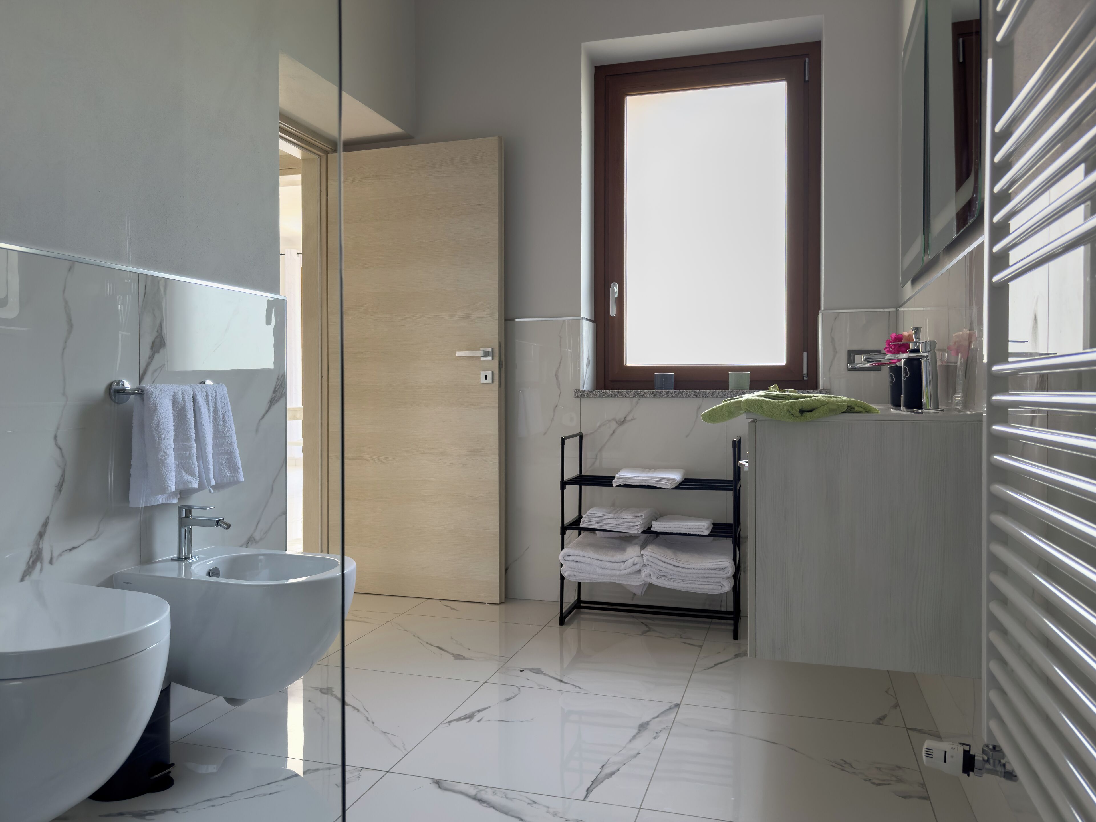 Een moderne badkamer met een marmeren vloer, een wastafel, een bidet en een raam.