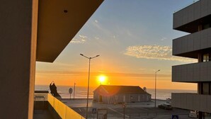 A coastal view with a sunset, a wooden building, and a modern building with balconies.