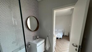 A modern bathroom with a toilet, sink, and mirror. There is a white towel hanging on the wall. The bathroom has a wooden floor and a patterned wall.