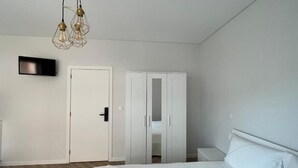 A bedroom with a bed, a wardrobe, a TV, and a hanging light fixture.