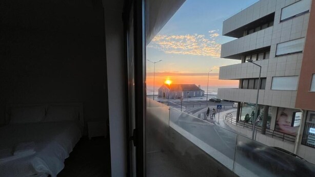 A bedroom with a view of a sunset over a cityscape.