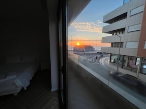 A bedroom with a view of a sunset over a cityscape.