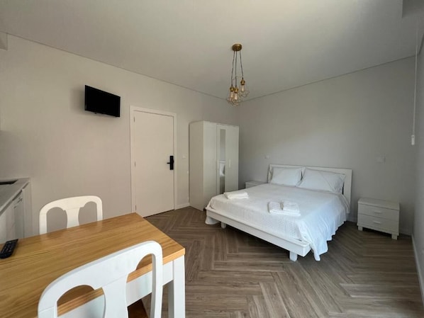 A bedroom with a bed, bedside tables, a wardrobe, a desk with chairs, and a television on the wall.