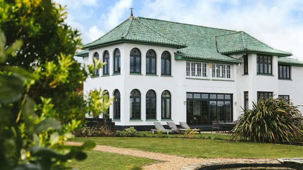 A two-story building with a green roof, large windows, and a well-maintained garden with a pond. - Christie Mansion - Luxury Cottages (Shanklin)