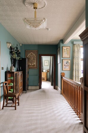 Ein Korridor mit einer gemusterten Decke, einer Chandelierleuchtre und einer Treppe mit hölzernem Geländer.