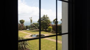 A view through a window with a garden, a pond, and a body of water in the distance. - Christie Mansion - Luxury Cottages (Shanklin)