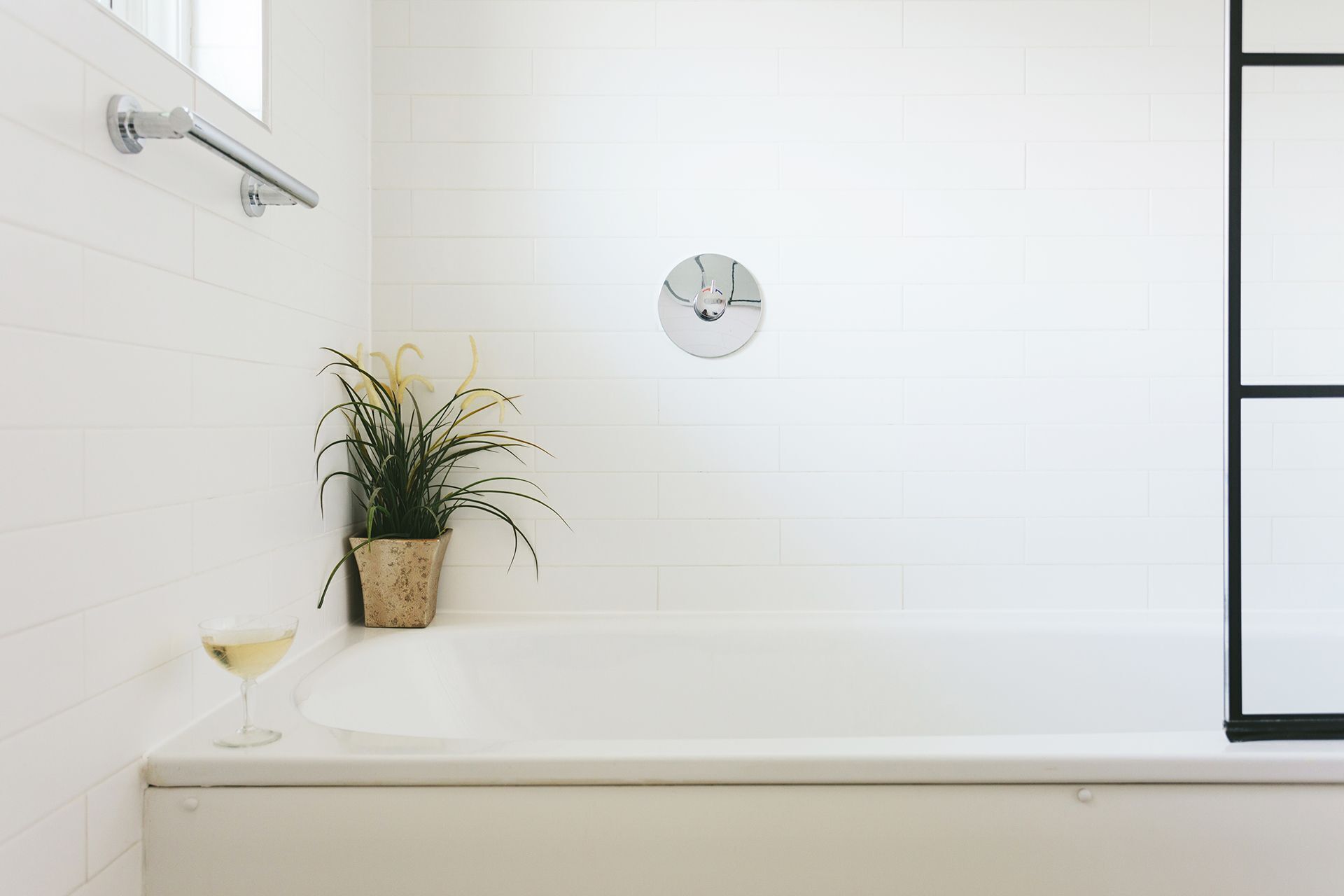 A white bathtub with a potted plant and a glass of white wine on the side.