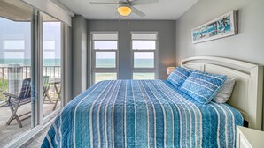 Un dormitorio con una cama grande, un ventilador de techo y vista al océano a través de amplios ventanales.