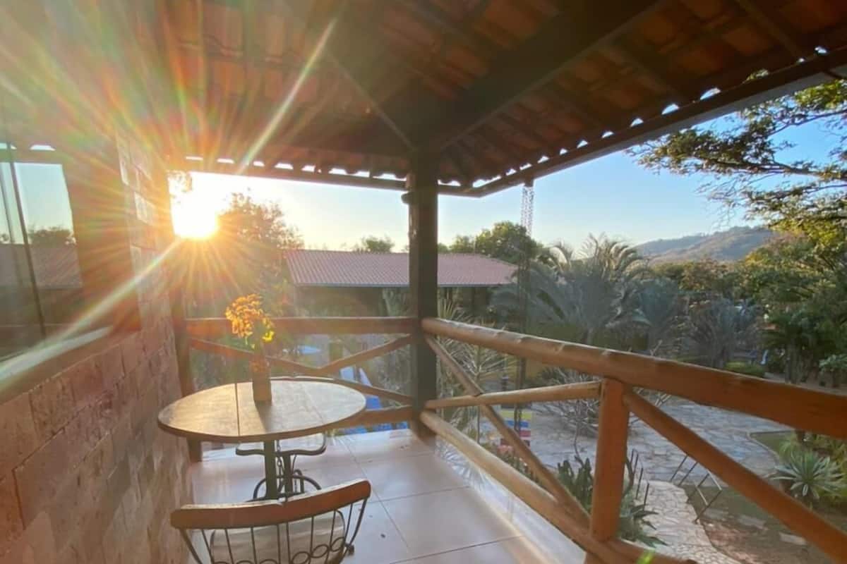 A balcony with a table and chairs, a view of the surrounding landscape, and a sun setting in the background.