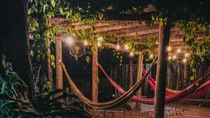 Una terraza de madera con un sendero de piedra que lleva a un espacio cubierto con hamacas y luces colgantes.