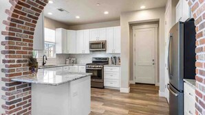 A modern kitchen with white cabinets, a central island, a stainless steel refrigerator, and a microwave. - The Ella:  Charming 1-level private home, community amenities. (Hurricane)