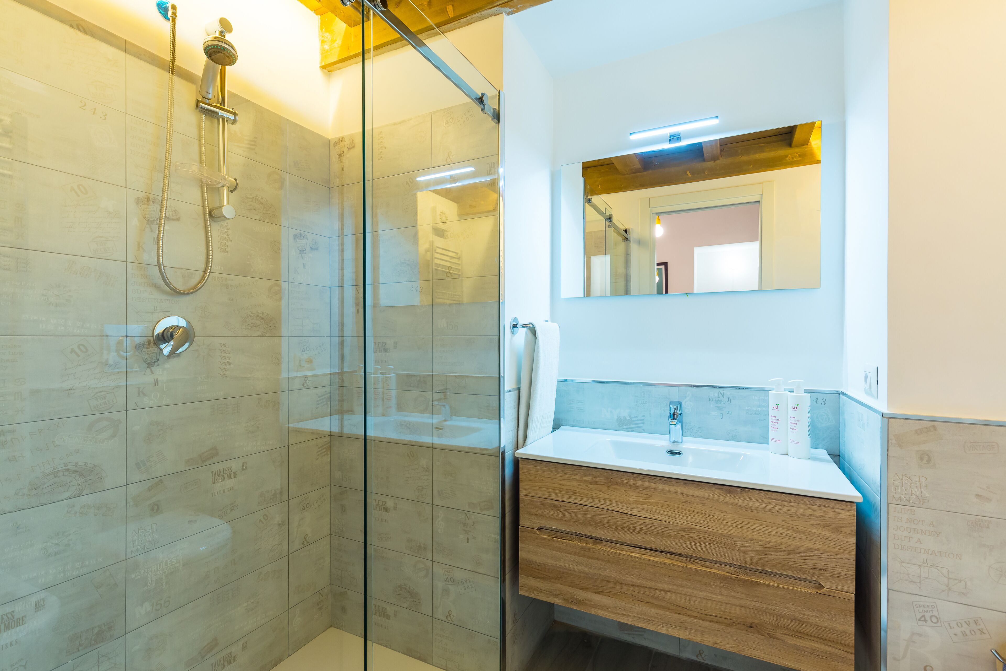 A modern bathroom with a glass shower enclosure, a wooden vanity, and a mirror above the sink.