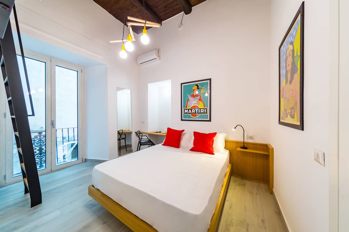 A modern hotel room with a large bed, a desk, and a balcony.