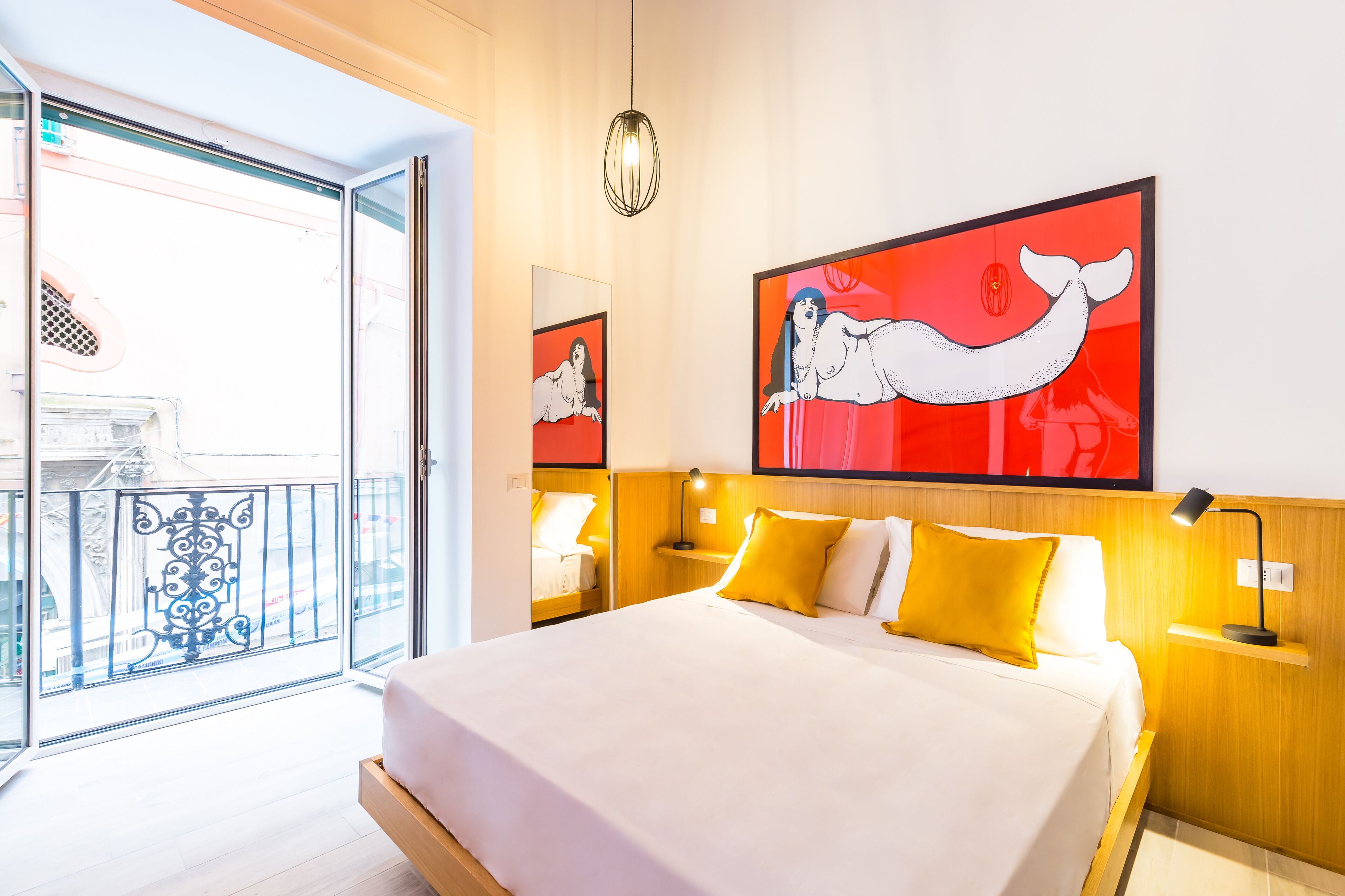 A hotel room with a large bed, a balcony with a view, and artwork on the wall.