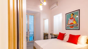 A hotel room with a large bed, red pillows, a desk, and a balcony.