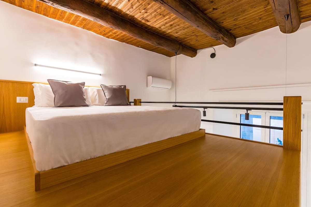 A bedroom with a wooden bed frame, white bedding, and a view of the city through a window.