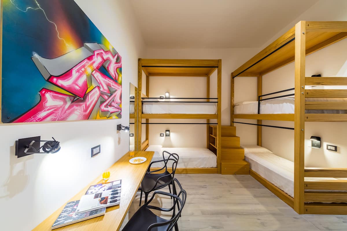 A compact room with bunk beds, a desk, chairs, a painting, and a small staircase.