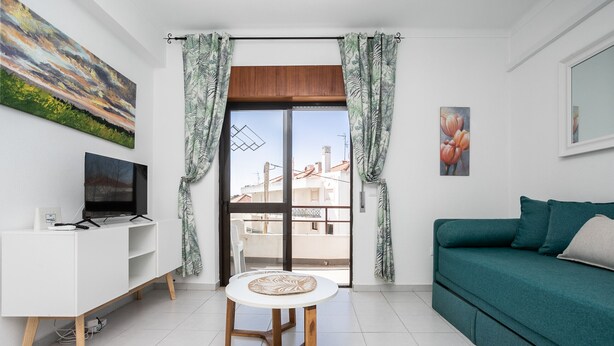 Una sala de estar moderna con un mueble blanco para el televisor, un sofá color turquesa, una mesa redonda y vistas a través de un gran ventanal corredizo.
