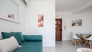 Una sala de estar con un sofá azul turquesa, una mesa de comedor con sillas y obras de arte en las paredes.