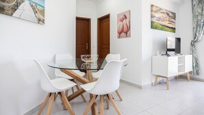 Un comedor moderno con una mesa de vidrio, sillas blancas, patas de madera y un armario blanco con un televisor.