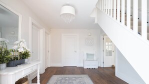 A spacious hallway with a wooden floor, a white console table with a basket, a large mirror, and a chandelier. - Arden House - Family Luxury in Lahinch! (Lahinch)