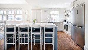 A modern kitchen with white cabinetry, a stainless steel refrigerator, and a central island with bar stools. - Arden House - Family Luxury in Lahinch! (Lahinch)