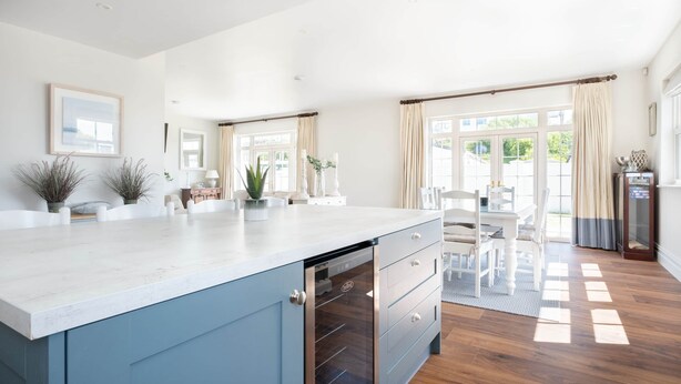 A modern kitchen with a built-in dishwasher, a dining area with a table and chairs, and large windows with curtains. - Arden House - Family Luxury in Lahinch! (Lahinch)