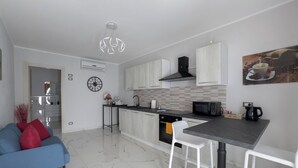 Une cuisine moderne avec un îlot central, des tabourets de bar blancs, un canapé bleu et une horloge au mur.