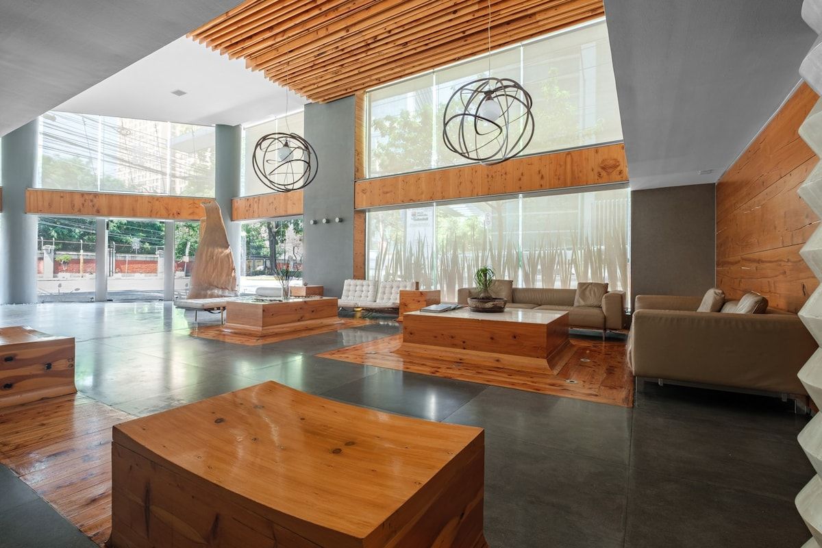A spacious lobby with wooden flooring, a central seating area, and large windows allowing natural light.