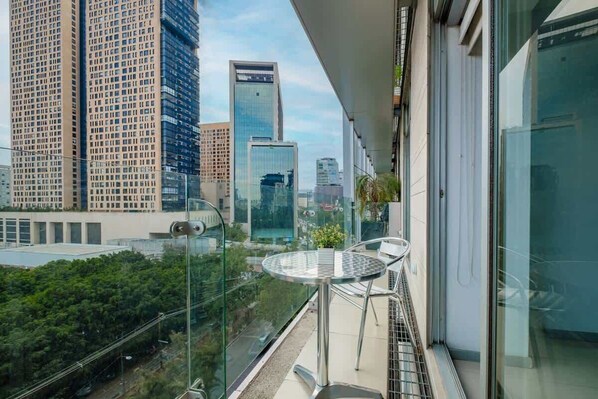 A balcony with a glass railing overlooking a cityscape with tall buildings.
