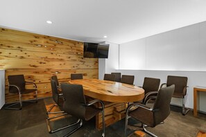 Une salle de conférence avec une table et des chaises en bois, un téléviseur à écran plat fixé au mur et un tableau blanc.