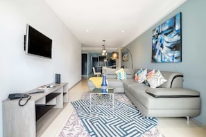 A modern living room with a flat-screen TV, a sofa, a coffee table, and a painting on the wall.