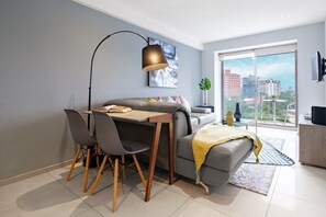 Un salon moderne comprenant un coin repas, un canapé, une table basse, une lampe et une vue sur la ville grâce à de grandes fenêtres.