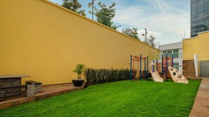 A well-maintained outdoor area with a yellow wall, a grassy lawn, and playground equipment. - Polanco 2BR  Skyline Balcony, Gym & Sauna (Mexico City)