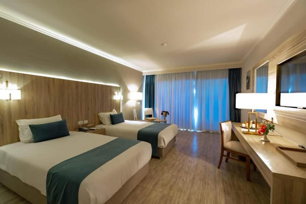 A hotel room with two beds, a desk, a chair, a TV, and a window with curtains.