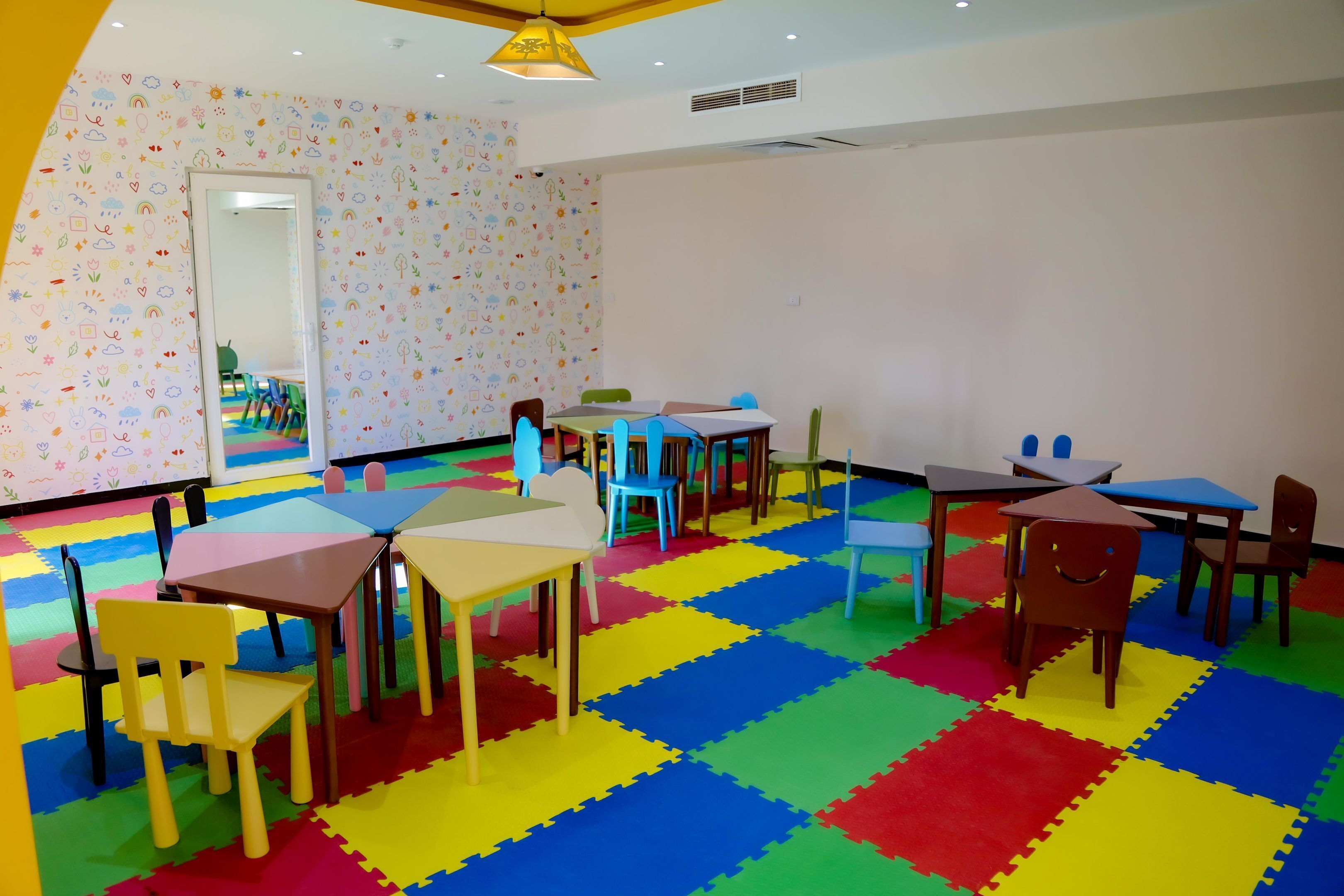 Ein Spielzimmer für Kinder mit bunten Schaumstoffmatten, Tischen, Stühlen und einem Spiegel an der Wand.