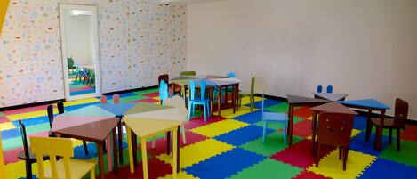Ein Spielzimmer für Kinder mit bunten Schaumstoffmatten, Tischen, Stühlen und einem Spiegel an der Wand.