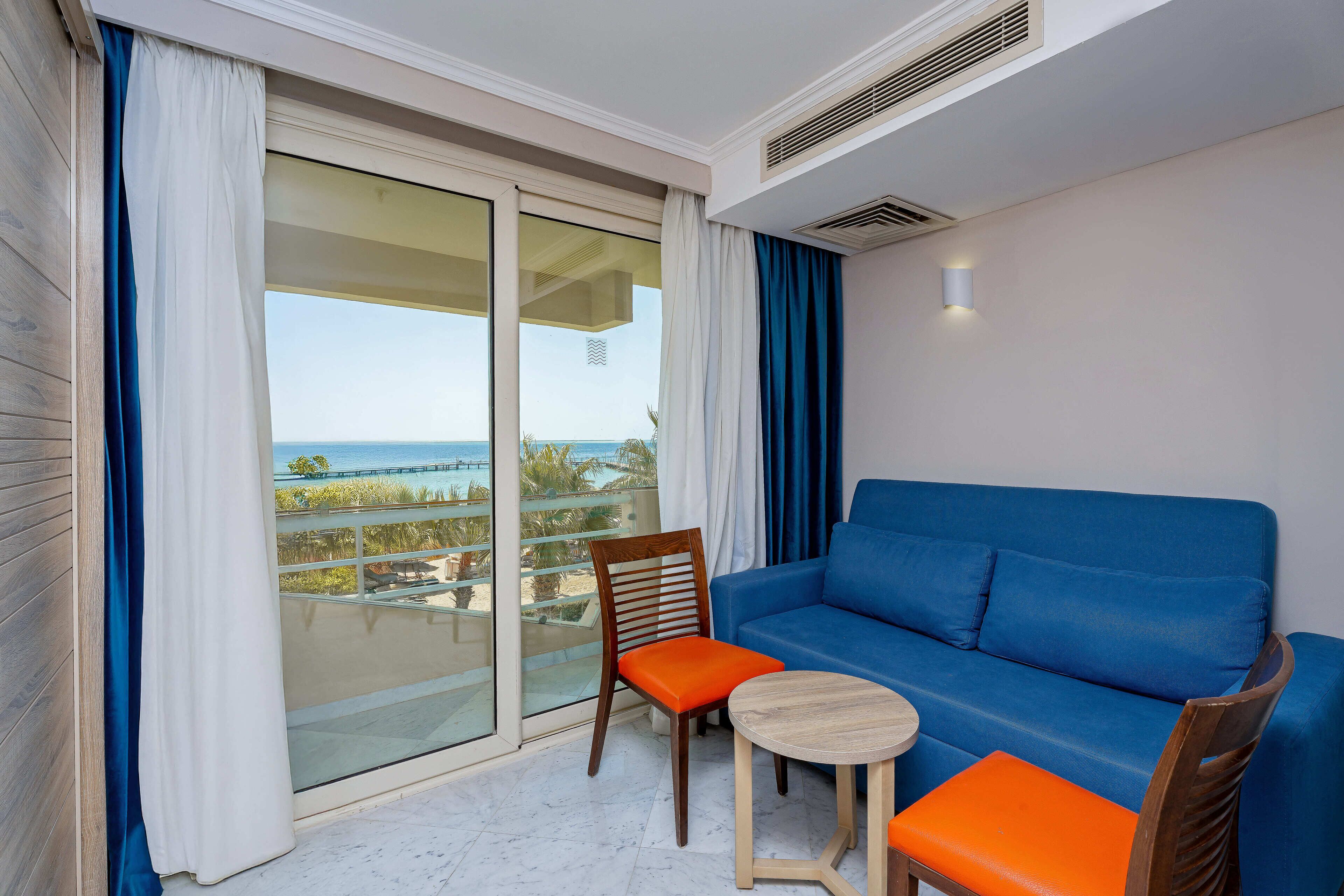 A balcony with a blue sofa, a wooden chair with an orange cushion, and a small round table.