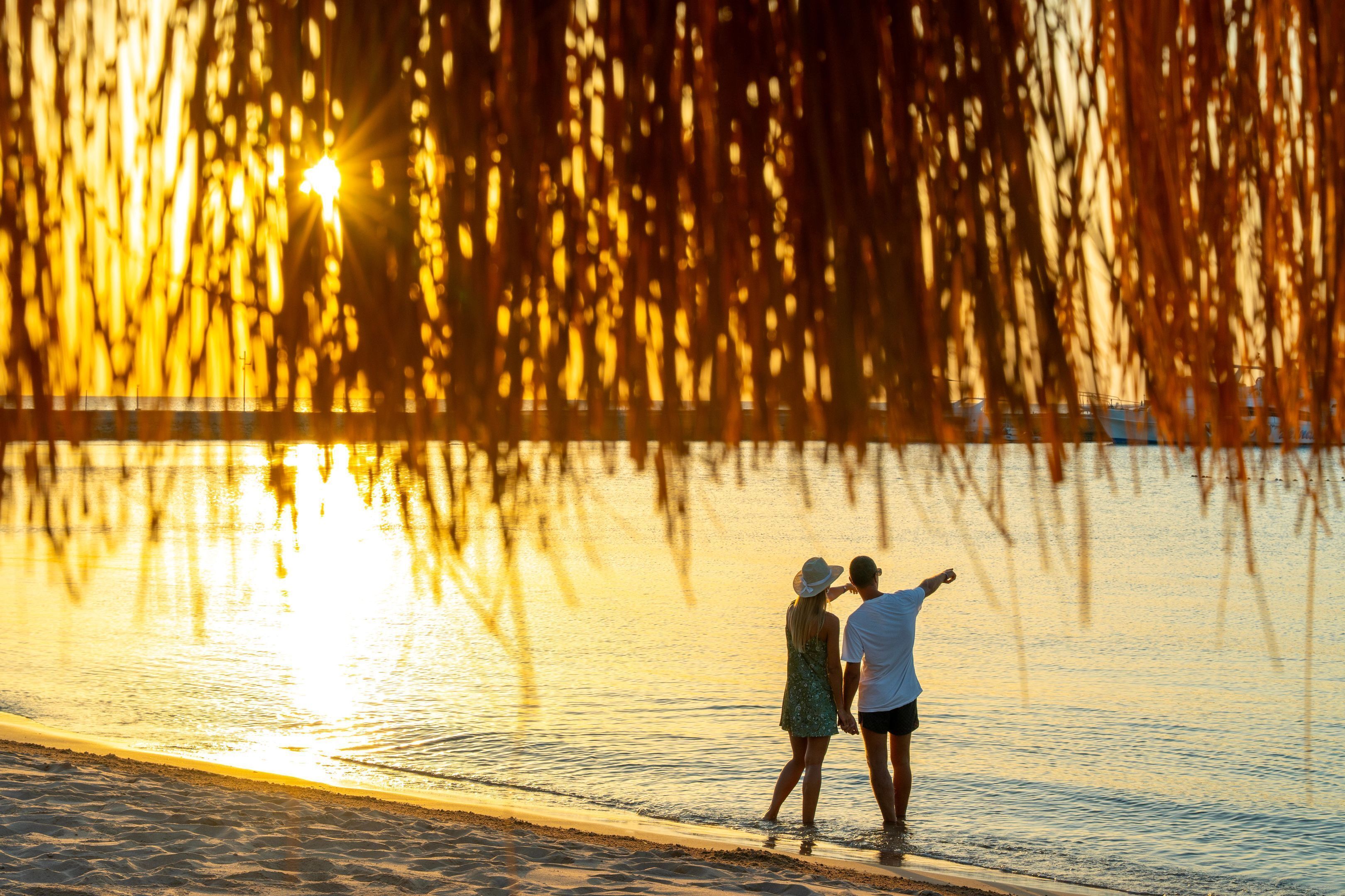 Dos personas junto a un cuerpo de agua al atardecer.
