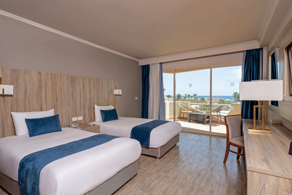 A hotel room with two beds, a desk, and a view of the city.