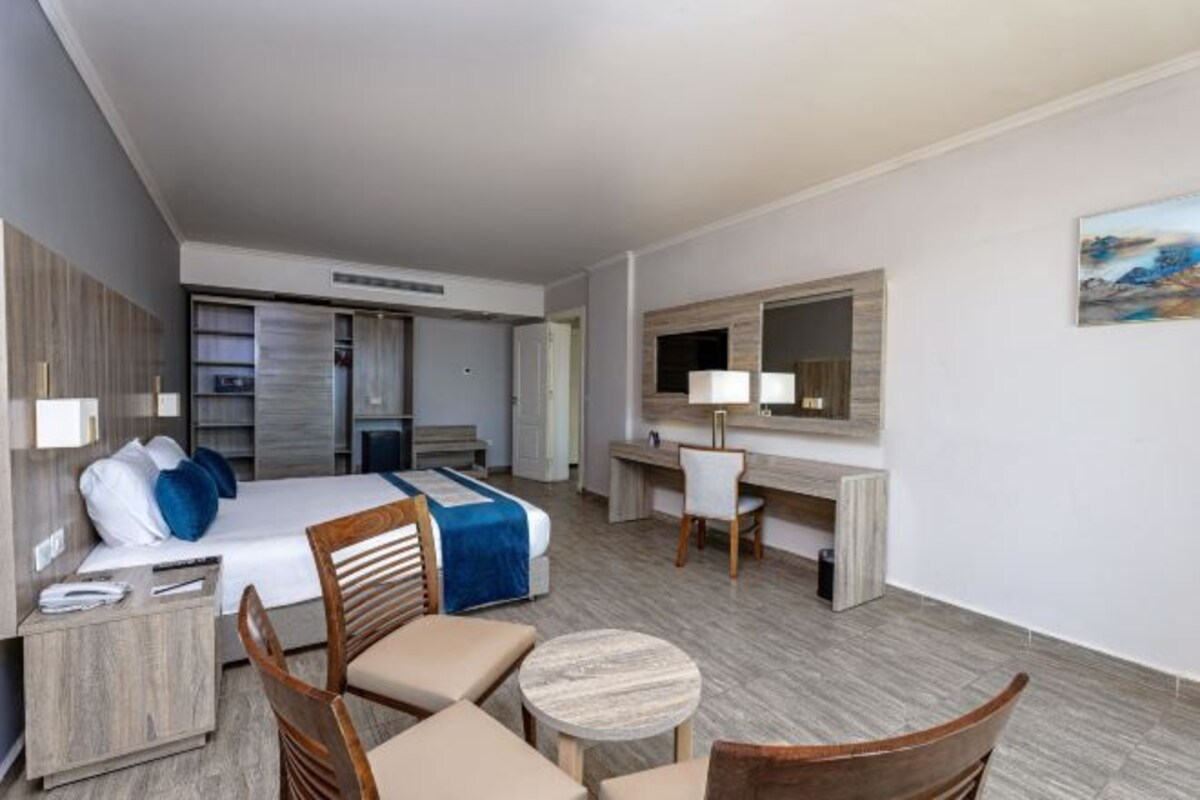 A hotel room with a bed, desk, chairs, and a small round table.