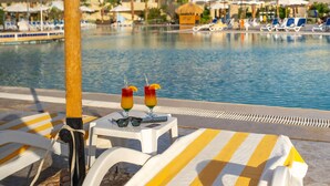 A poolside area with lounge chairs, a table with drinks, and a view of a hotel building in the background. - Seven Seas Jolie Bay - Ultra All Inclusive (Safaga)
