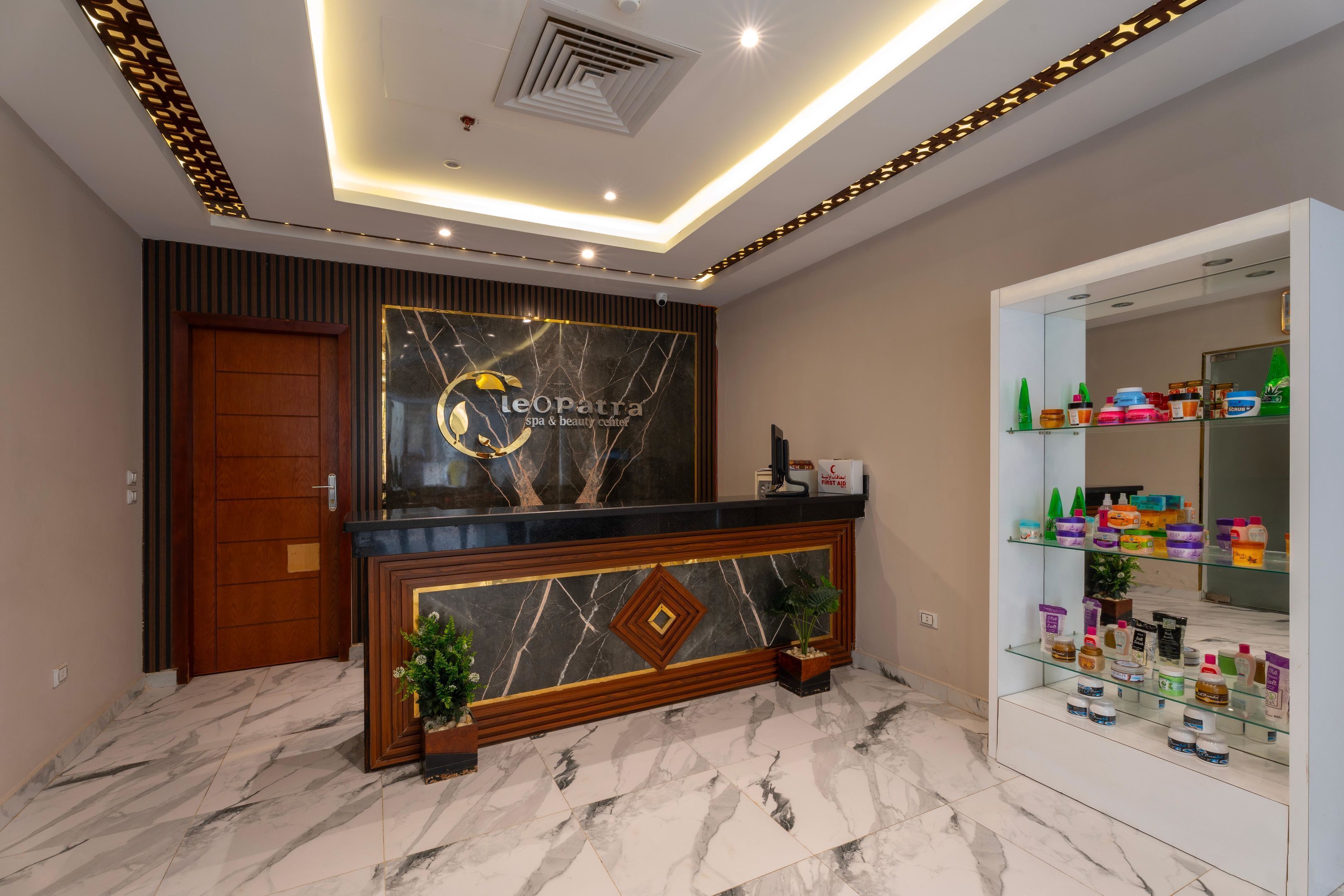 Zona de recepción con piso de mármol, un mostrador, una puerta de madera y un panel en la pared que muestra varios productos.