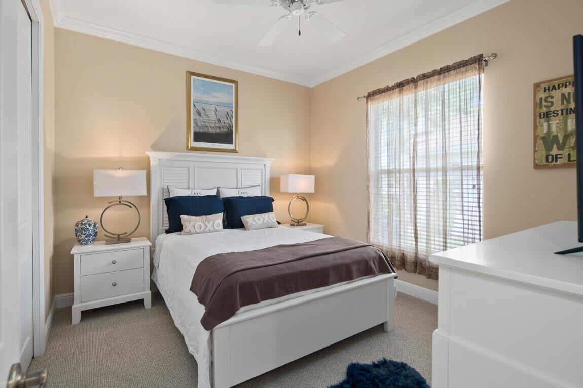 A bedroom with a bed, nightstands, a dresser, a ceiling fan, and a window with curtains.