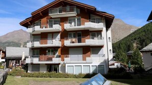 Un edificio de varios pisos con balcones, techo plano y montañas al fondo.