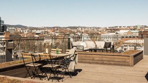A rooftop terrace with outdoor seating, a view of a cityscape, and a wooden deck. - Løkka City Apartments (Oslo)