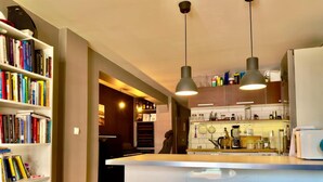 A modern kitchen with a central island, pendant lights, and a bookshelf filled with books. - Løkka City Apartments (Oslo)