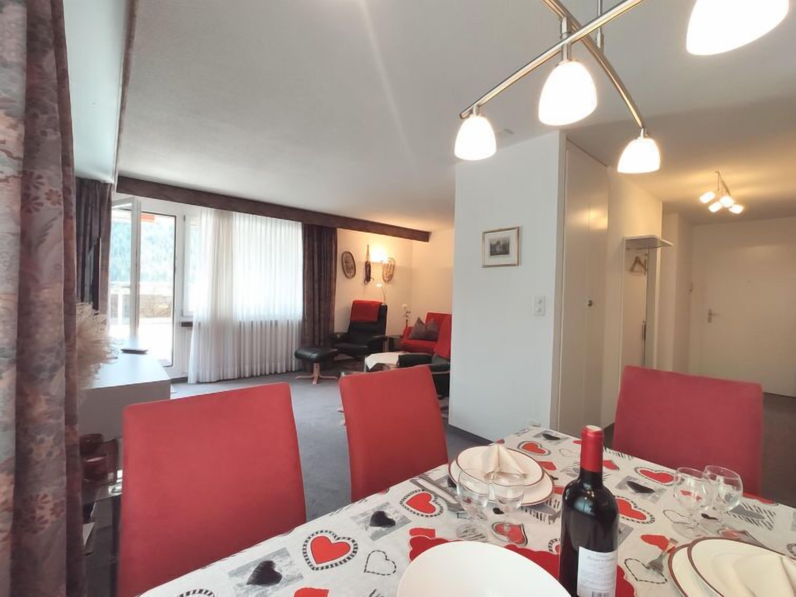 Un coin repas avec une table dressée pour quatre personnes, des chaises rouges et un lustre.